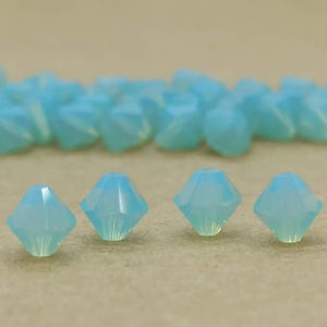 Könnte beinhalten: Nahaufnahme von vier hellblauen Kristallperlen mit facettiertem Design. Die Perlen sind in einer Reihe auf einer braunen Oberfläche angeordnet.