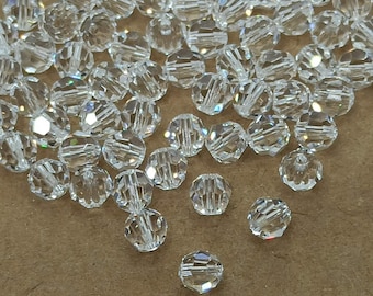 May include: A large quantity of clear glass beads with a faceted design. The beads are scattered on a brown surface.