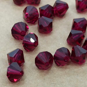 May include: A group of ruby red faceted glass beads. The beads are small and have a pointed shape.