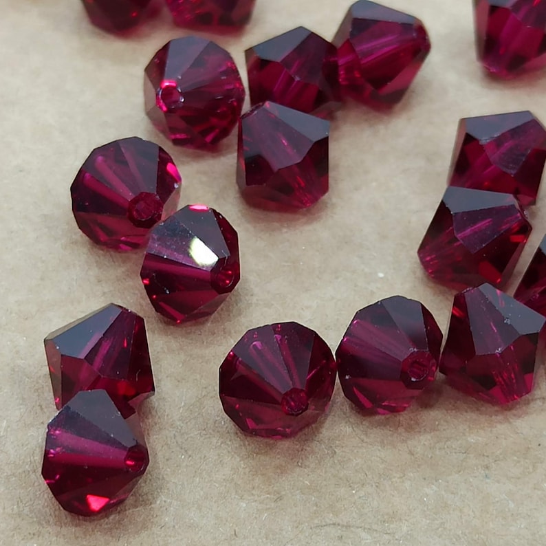 May include: A group of ruby red faceted glass beads. The beads are small and have a pointed shape.