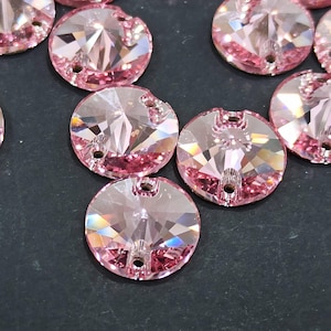 Puede incluir: Primer plano de varias cuentas de cristal redondas, facetadas, de color rosa claro. Cada cuenta tiene dos agujeros para ensartar y una parte posterior plana. Los cristales reflejan la luz, creando un efecto brillante. Las cuentas están dispersas sobre una superficie oscura.