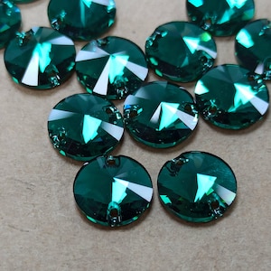 May include: Close-up of several emerald green, faceted crystal rhinestones. Each round stone has a flat back and two small holes for attaching. The crystals reflect light, creating bright white and green highlights.