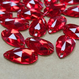May include: A collection of vibrant red, teardrop-shaped faceted crystals. Each crystal features a smooth, polished surface with multiple geometric facets that reflect light, and includes a small, pre-drilled hole at the narrow end for attachment.