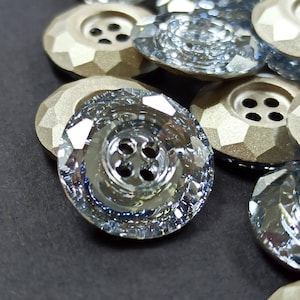 May include: Close-up of several decorative buttons. Some buttons are clear with a faceted design, while others are a metallic gold color with a faceted design. Each button has four holes for sewing.