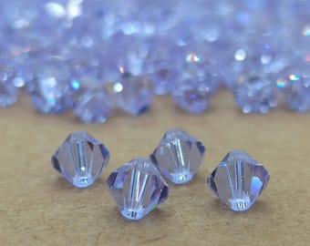 May include: Four clear, faceted, lavender-colored glass beads. The beads are shaped like a pyramid with a pointed top and a flat base. The beads are arranged in a row on a brown surface.