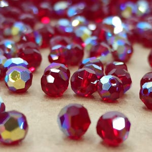 Könnte beinhalten: Nahaufnahme einer Ansammlung roter, irisierender Glasperlen. Die Perlen sind rund und haben eine facettierte Oberfläche.