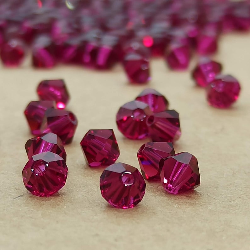 May include: A close-up of a group of small, faceted, ruby red glass beads. The beads are arranged on a brown surface.