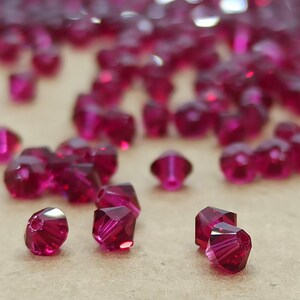 May include: A close-up of a pile of small, faceted, ruby red glass beads. The beads are scattered on a brown surface.