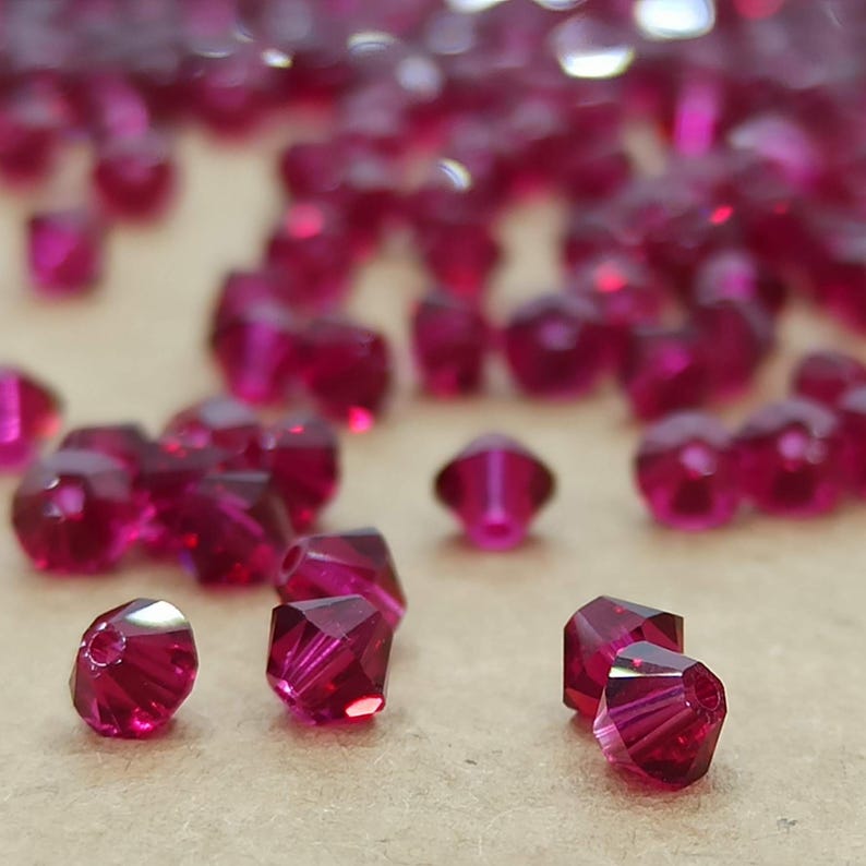 May include: A close-up of a pile of small, faceted, ruby red glass beads. The beads are scattered on a brown surface.