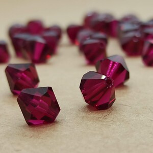 May include: A close-up of a group of small, faceted, ruby red glass beads. The beads are scattered on a brown surface.