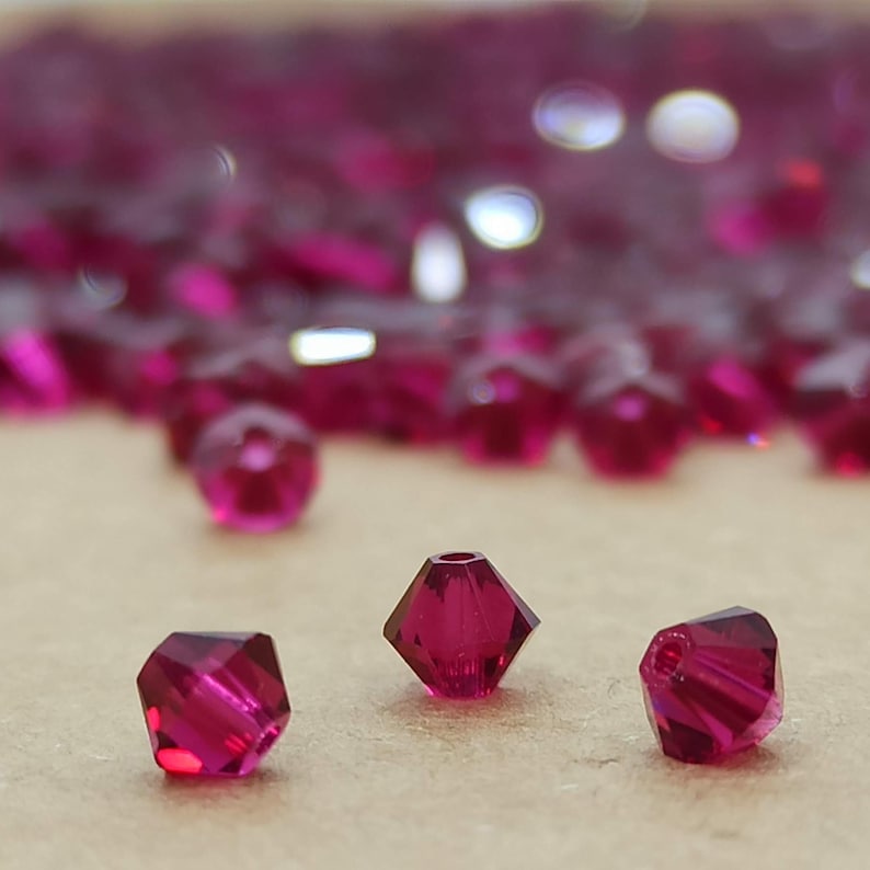May include: Close-up of three pink faceted glass beads. The beads are small and have a pointed shape.