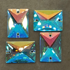 May include: Four iridescent blue square-shaped rhinestones with two holes each. The rhinestones have a rainbow effect and are perfect for crafting and jewellery making.