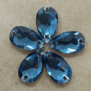 May include: Five blue teardrop-shaped rhinestones arranged in a flower pattern. Each rhinestone has a faceted surface and two small holes at the top for attaching. The rhinestones are a deep, reflective blue color.