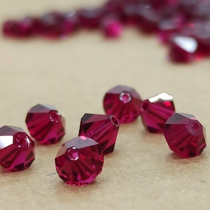 May include: A close-up of a group of small, faceted, ruby red glass beads. The beads are scattered on a brown surface.