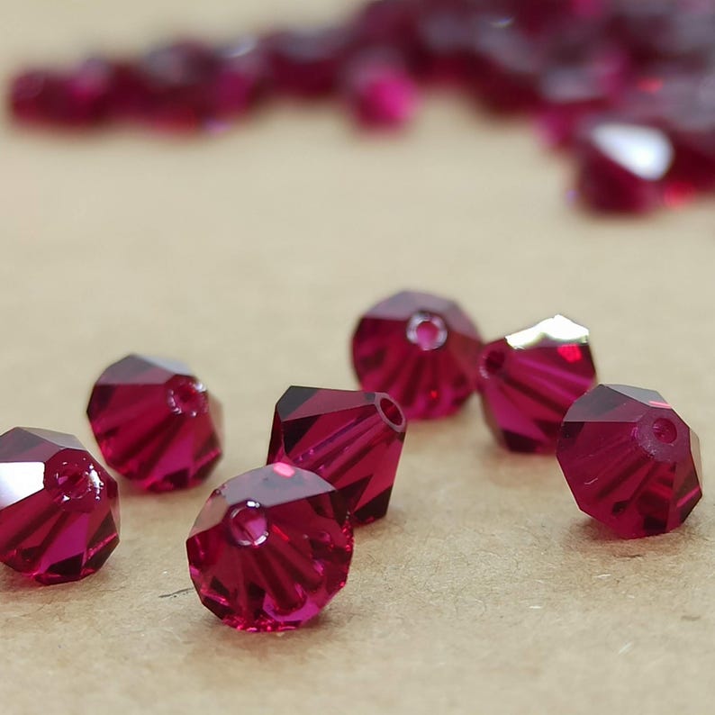 May include: A close-up of a group of small, faceted, ruby red glass beads. The beads are scattered on a brown surface.