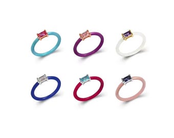 May include: Six colourful silicone rings with a small rectangular gemstone set in a gold setting. The rings are in the colours turquoise, purple, white, blue, red, and pink.