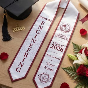 May include: A graduation cap, sash, diploma, and flowers are arranged on a wooden surface. The white sash has burgundy trim and reads "Software Engineering" and "Class of 2026." A bouquet of red roses and white lilies adds a celebratory touch.