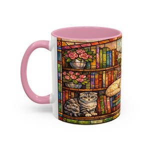 Puede incluir: Taza de cer&aacute;mica blanca con interior y asa rosas. La taza presenta un colorido dise&ntilde;o de vidriera de una estanter&iacute;a con libros, rosas rosas y un gato atigrado gris. Un dise&ntilde;o acogedor y encantador para los amantes de los gatos.