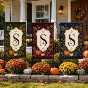 May include: Three rectangular garden flags in dark green, deep red, and navy blue, each featuring a central cream-colored shield with a large black letter S, surrounded by autumn leaves, berries, and small pumpkins on a black metal stand.