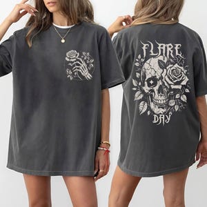 May include: A dark gray oversized t-shirt with a skull and rose graphic on the back and a skeleton hand holding a rose graphic on the front. The text "FLARE DAY" is printed below the skull graphic.
