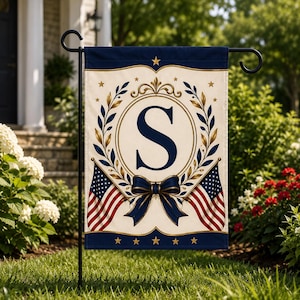 May include: A rectangular garden flag featuring a cream-colored background with a large navy blue letter S centered inside a gold laurel wreath. The design includes two American flags, a navy blue bow, and gold stars on navy blue borders.