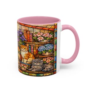 Puede incluir: Taza de cer&aacute;mica blanca con interior y asa rosas. La taza presenta un dise&ntilde;o de vidriera con dos gatos, libros y flores en macetas en tonos naranja, gris, rosa, azul y morado. La taza es de tama&ntilde;o est&aacute;ndar.