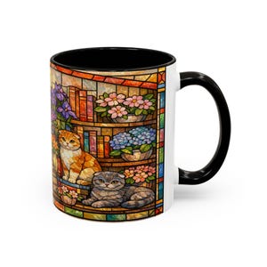 Puede incluir: Taza de cer&aacute;mica blanca con interior y asa negros. La taza presenta un colorido dise&ntilde;o de vidriera con dos gatos, libros y flores. El dise&ntilde;o incluye tonos naranja, gris, rosa, azul y morado.