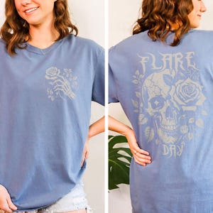 May include: A light blue t-shirt with a white skull and rose graphic on the back. The text "FLARE DAY" is printed below the graphic.