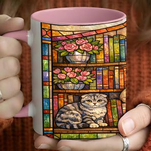 Puede incluir: Taza de cer&aacute;mica blanca con interior y asa rosas. La taza presenta un colorido dise&ntilde;o de vidrieras de una estanter&iacute;a con rosas rosas en macetas plateadas y un gato atigrado gris. El dise&ntilde;o incluye libros y un borde de vidriera.