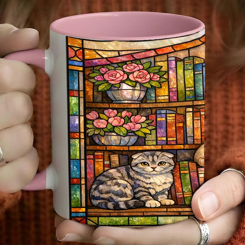 Puede incluir: Taza de cer&aacute;mica blanca con interior y asa rosas. La taza presenta un colorido dise&ntilde;o de vidrieras de una estanter&iacute;a con rosas rosas en macetas plateadas y un gato atigrado gris. El dise&ntilde;o incluye libros y un borde de vidriera.
