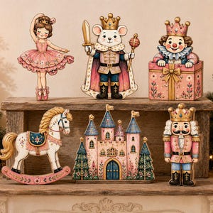 Peut inclure: Un ensemble de six figurines décoratives en bois représentant une ballerine, un roi souris avec épée et sceptre, un clown dans un cadeau, un cheval à bascule, un château et un casse-noisette, peints dans des tons de rose, bleu et or.