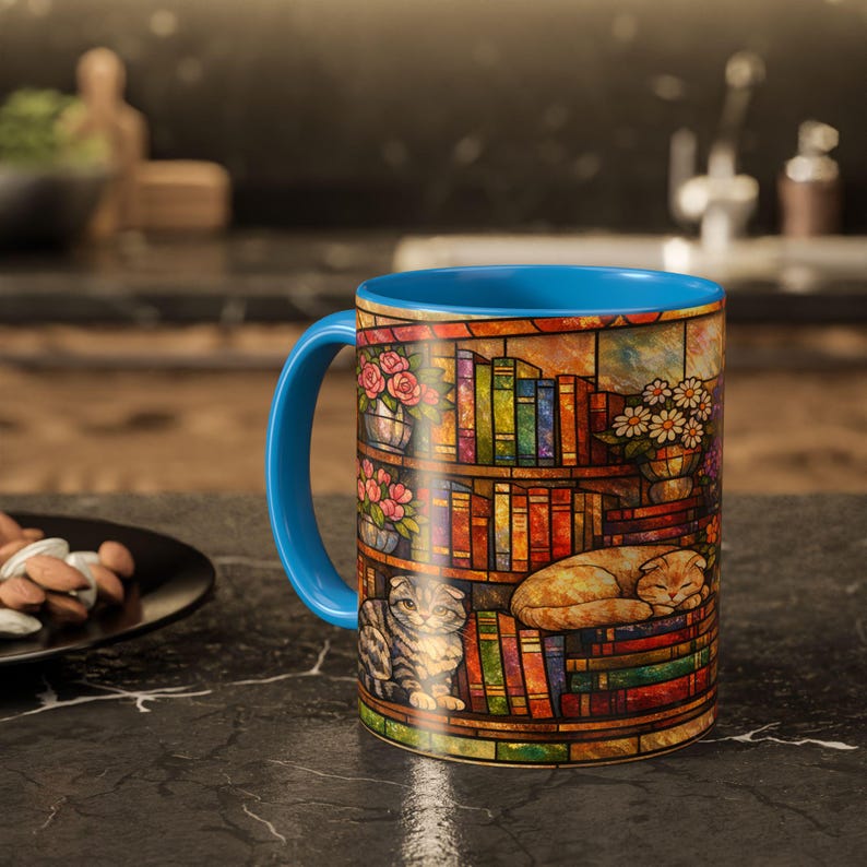 Puede incluir: Una taza de caf&eacute; de cer&aacute;mica con asa e interior azules. La taza presenta un dise&ntilde;o de vidriera de una estanter&iacute;a con libros, flores y dos gatos. La taza est&aacute; sobre una superficie negra.