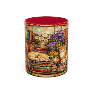 Puede incluir: Taza de cer&aacute;mica con un dise&ntilde;o de vidriera que representa una escena de biblioteca con libros, flores y dos gatos. El interior de la taza es rojo. El dise&ntilde;o envuelve la taza, mostrando un tema art&iacute;stico y acogedor.