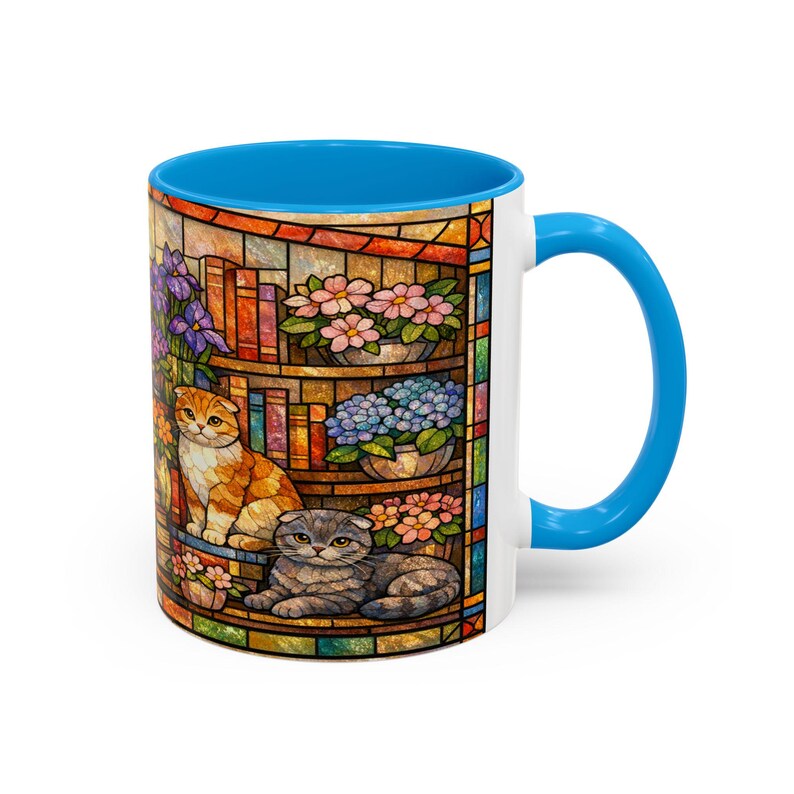 Puede incluir: Taza de cer&aacute;mica blanca con interior y asa azules. La taza presenta un dise&ntilde;o de vidriera con dos gatos, libros y flores en macetas en tonos naranja, azul, rosa y morado.
