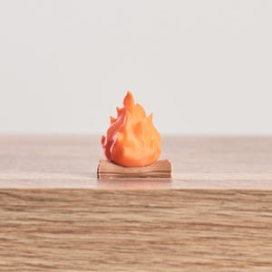 May include: A miniature orange flame sculpture atop a small, brown log. The flame is a vibrant orange color, with detailed peaks and valleys. The log appears to be made of wood, with visible grain. The sculpture is likely a decorative item or a toy.