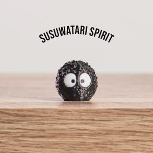 May include: A black, spherical figure with large white eyes and the text "SUSUWATARI SPIRIT" above it. The figure has a textured surface and sits on a wooden surface.