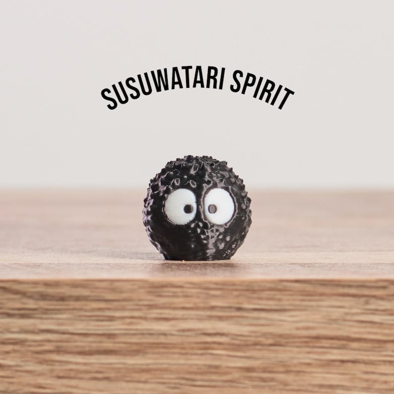 May include: A black, spherical figure with large white eyes and the text "SUSUWATARI SPIRIT" above it. The figure has a textured surface and sits on a wooden surface.