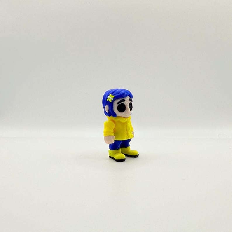 May include: A small figurine of a character with blue hair, a yellow jacket, blue pants, and yellow boots. The character has a flower in their hair and large black eyes. The figurine is standing on a white surface.