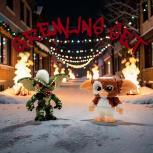 May include: Two Gremlins figures stand on a snowy street, with the text "GREMLINS SET" above them. One figure is green with a white mohawk and red eyes. The other is brown and white with large ears. The background features Christmas lights.