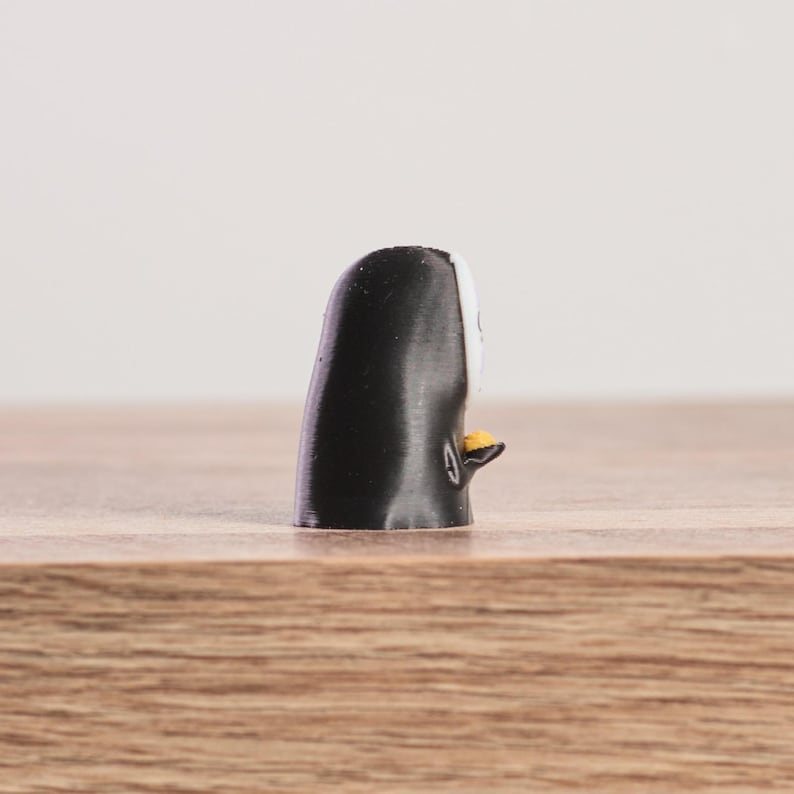 K&ouml;nnte beinhalten: Kleine, schwarz-wei&szlig;e Pinguin-Figur mit gelbem Schnabel und F&uuml;&szlig;en. Der Pinguin steht auf einer Holzoberfl&auml;che. Die Figur ist ein dekoratives Objekt.