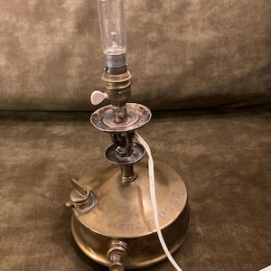 Op de afbeelding: Vintage messing tafellamp met een heldere glazen lamp. De lamp heeft een ronde voet met een schakelaar en een wit snoer. De lamp is gemaakt van messing en heeft een klassiek ontwerp.