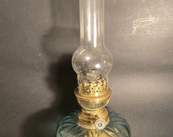 May include: Antique oil lamp with a clear glass chimney and a teal and gold-colored glass reservoir. The lamp has a brass burner and base, and sits on a black base. A vintage lighting fixture.