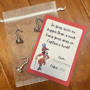 May include: A red card with a cartoon image of Captain Hook and the text "In your room no bigger than a nook. Hang your gear on Captain's hook!"  The card also includes the text "from The Smith Family Cabin 2519". Three silver hooks are included in the image.
