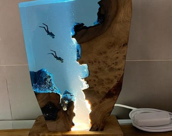 Könnte beinhalten: Eine Holzlampenbasis mit einem klaren blauen Harzeinsatz, der Silhouetten von Tauchern zeigt. Das Harz wird von hinten beleuchtet, wodurch ein leuchtender Effekt entsteht.
