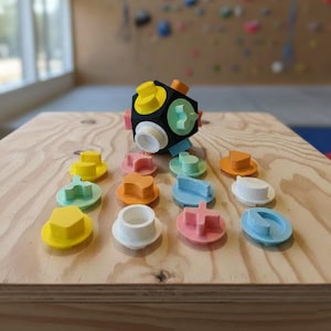 May include: A black, multi-colored geometric puzzle with various shapes and colors, including yellow, orange, green, and pink. The puzzle is on a wooden surface, with several detached pieces nearby.