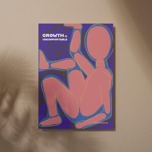 May include: A poster with a pink figure in a seated position against a dark blue background. The figure is outlined in yellow. The text "GROWTH IS UNCOMFORTABLE" is in white at the top. The artist's signature is in the bottom right corner.