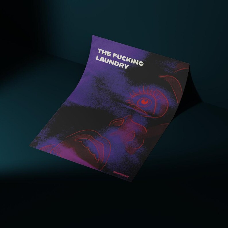 Op de afbeelding: Een poster met de tekst "THE FUCKING LAUNDRY" in het wit, met een gestileerd gezicht in rood en paars. De achtergrond is een mix van zwart, paars en blauw. De poster leunt tegen een donkerblauwe muur.