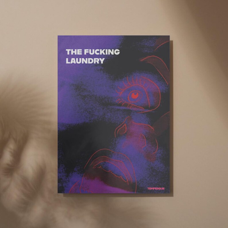 Op de afbeelding: Een poster met de tekst "THE FUCKING LAUNDRY" in het wit. Het kunstwerk toont een gezichtsomtrek in rood tegen een donkerpaarse en zwarte achtergrond. De naam van de kunstenaar, TEMPERGUE, staat rechtsonder.