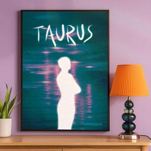 Può includere: Una stampa artistica incorniciata con la parola "TAURUS" in scrittura bianca sopra una silhouette bianca di una persona con le braccia incrociate. Lo sfondo è una scena acquatica turchese e rosa. Una lampada arancione con paralume plissettato è su un tavolo di legno.