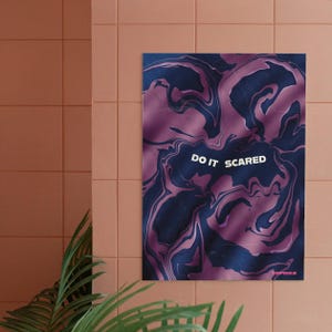 May include: A poster with a swirling abstract design in shades of purple and navy blue. The words "DO IT SCARED" are in white, centered on the poster. The poster is hanging on a peach-colored tiled wall.